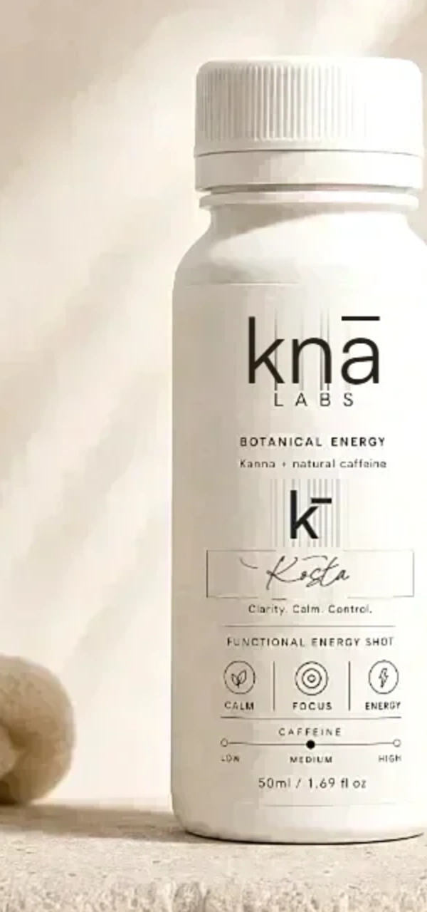 The knā Kosta shot: a white bottle with a stamp-set label, standing on stone.