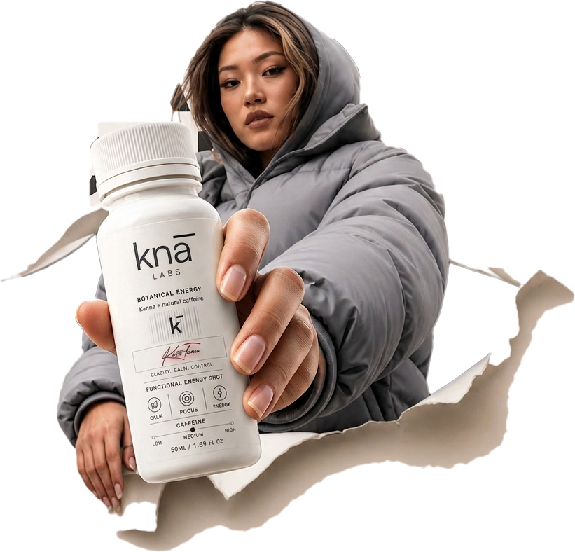 A figure in a grey down jacket pushes a knā bottle forward through torn paper.