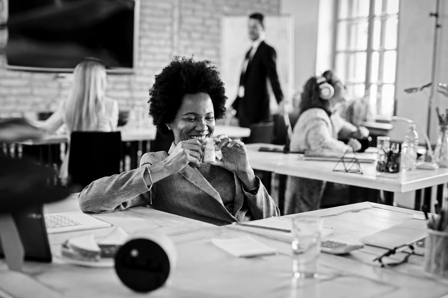 A desk-side ritual in a daylight studio office, black and white.